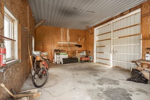 Metal-roofed garage interior with exposed framing, storage shelving, and a bicycle