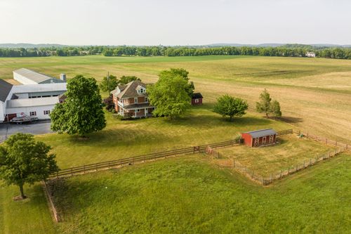 Aerial close view of a brick farmhouse shaded by a large tree beside open farmland