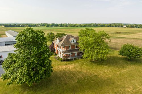 Aerial view of a brick farmhouse framed by mature trees next to a barn complex