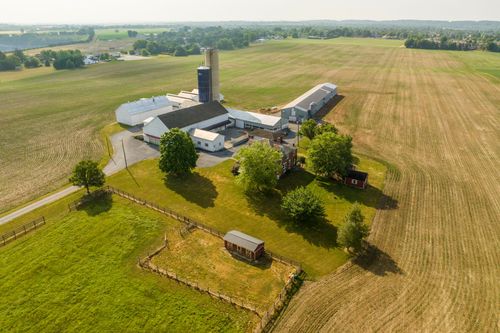 Aerial view of a farm complex with silo, barns and a red outbuilding beside a brick farmhouse