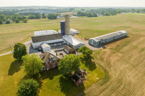 Aerial view of a farm complex with silo, tall grain structure and barns beside a brick farmhouse