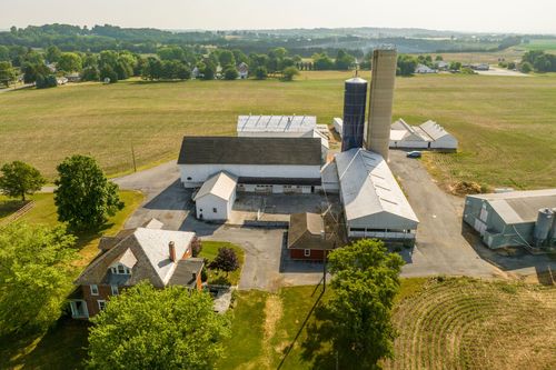Gravel driveway lined with trees and wood fencing leading up to a farm complex with a silo