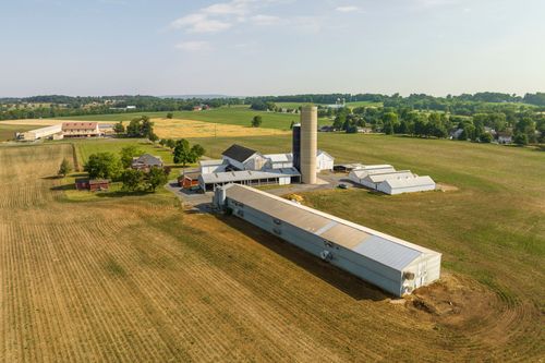 Brick two-story farmhouse with a wraparound porch beside a barn and silo