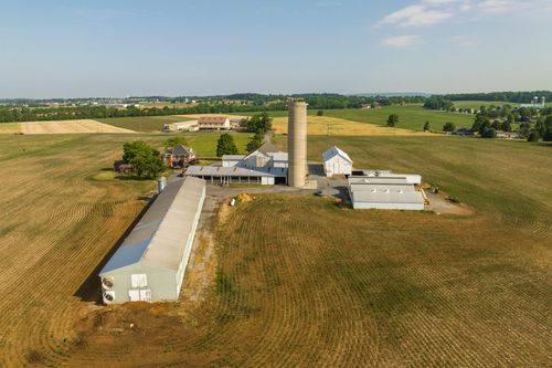 Brick two-story farmhouse with a wraparound porch and dormer windows beside a barn complex