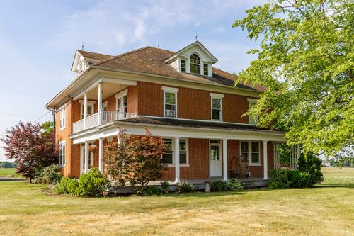 Front exterior of a brick farmhouse with a covered wraparound porch and dormer window
