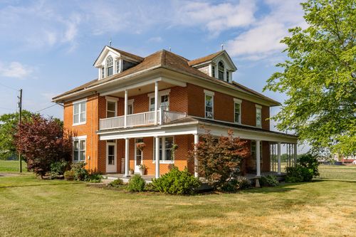 Brick farmhouse exterior framed by a mature red-leaf tree and covered porch