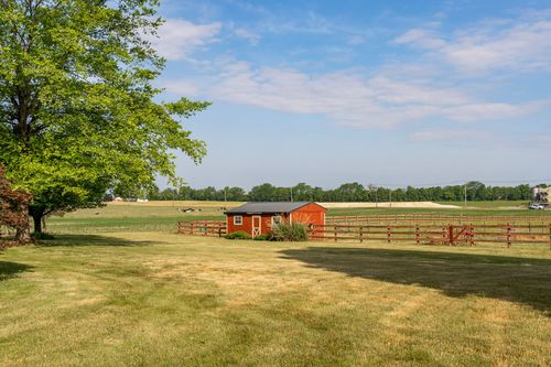 Red storage shed and wood fence beneath a large shade tree in an open pasture