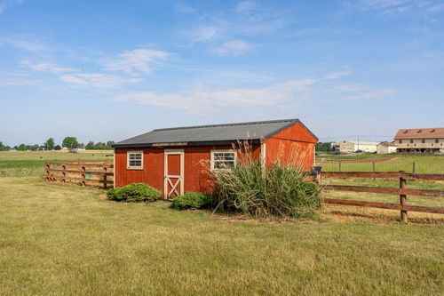 Red board-and-batten shed with double doors set in tall grass along a wood fence
