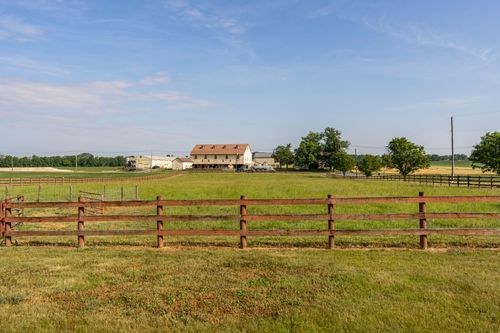 Wood-fenced pasture with a farmhouse and barn complex visible across the field