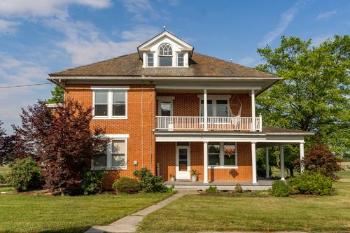 Brick farmhouse exterior with wraparound porch and turret-style dormer