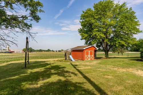 Red storage shed and play slide beneath a large shade tree beside open fields