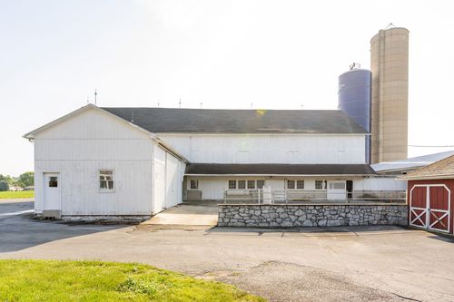 Long white dairy barn with a stone-walled covered breezeway and silo