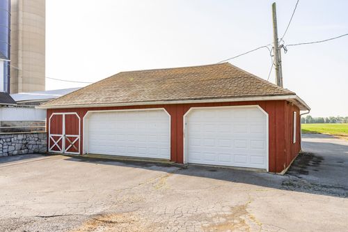 Red pole building with two white sliding garage doors on a gravel drive