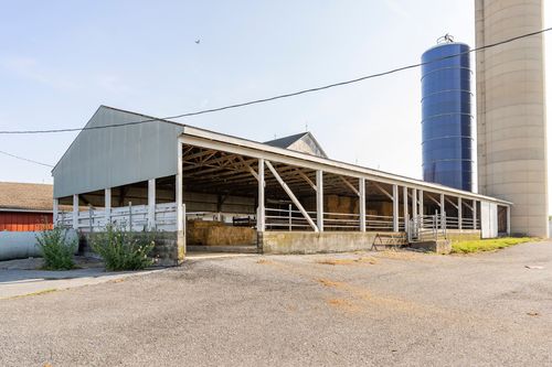 Open-sided pole barn shelter with a blue grain silo in the background