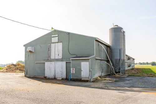 Green-gray sided barn exterior with a roof vent fan and white doors
