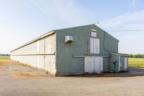 Long green-gray barn exterior with white doors and a ladder leaning against the wall