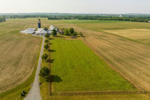 Aerial view of a farmstead with silo, barns and a tree-lined driveway bordered by wood fencing