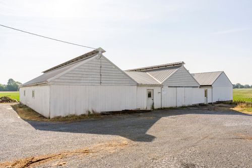 Long white barn exterior with a silo and stone-walled covered walkway