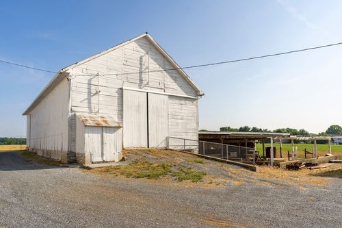 White barn exterior with a rusty-roofed lean-to and covered livestock pen
