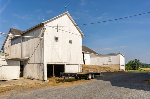 White barn exterior with a flatbed trailer parked in the gravel yard