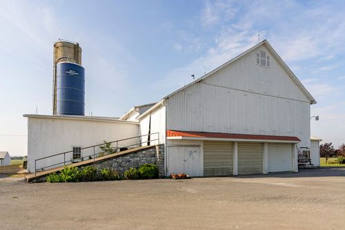 Barn complex with tan silo, stone ramp and red-trimmed garage doors near a farmhouse