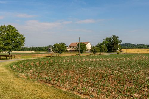 Wood-fenced pasture with cornfield in the foreground and a farmhouse in the distance