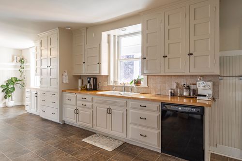 Long kitchen with white cabinetry, a bay window and tile flooring