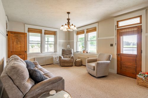 Living room with a chandelier, upholstered chairs and a wood front door with sidelights