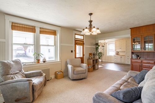 Living room with sofas and a chandelier opening to a kitchen with a wood hutch