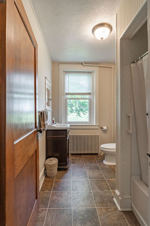 Bathroom with a dark wood vanity, radiator and a tub concealed by a patterned shower curtain