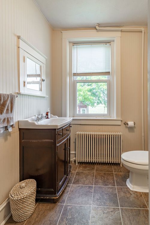 Bathroom with a dark wood vanity, medicine cabinet mirror, radiator and window