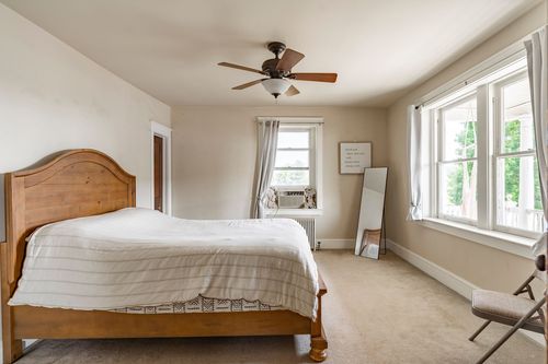 Bedroom with a wood bed, ceiling fan, window air conditioner and a full-length mirror