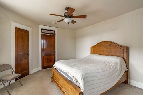 Bedroom with a wood bed, ceiling fan, two paneled wood doors and a folding chair