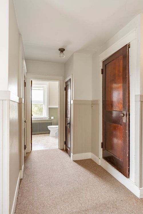 Hallway with a wood door open to a green-tiled bathroom, staircase newel post in the foreground