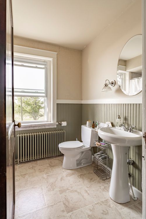 Bathroom with green beadboard wainscoting, pedestal sink, oval mirror and radiator