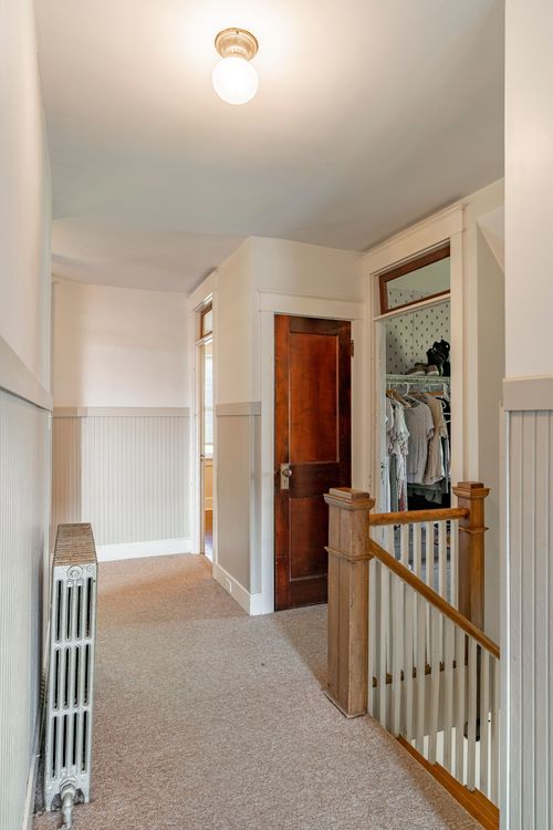 Hallway with a wood door open to a walk-in closet, carpet runner and staircase railing