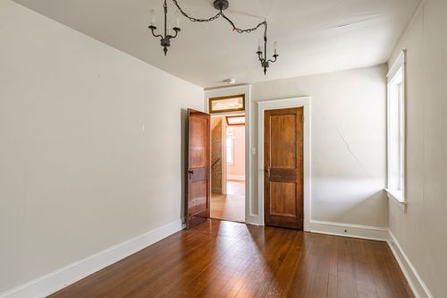 Empty room with wood floors, a chandelier and two wood doors open to a hallway