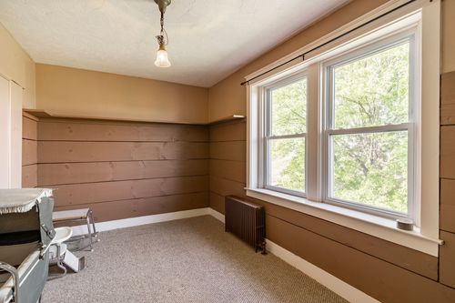 Empty room with wood plank wainscoting, a pendant light and a window overlooking trees