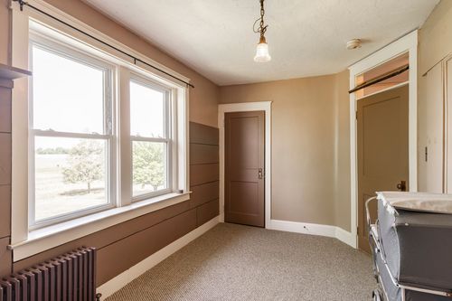 Cozy bedroom with tan walls, radiator, and a large window overlooking open farmland