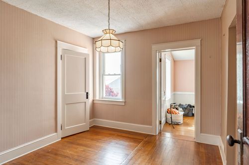 Empty bedroom with hardwood floors, a pendant light, and a doorway to a hallway