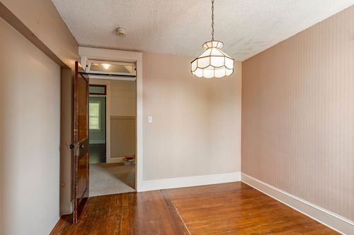 Unfurnished room with hardwood floors, a pendant chandelier, and an open doorway