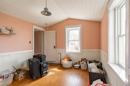 Attic room with vaulted ceiling, pink walls, wood floors, and open shelving