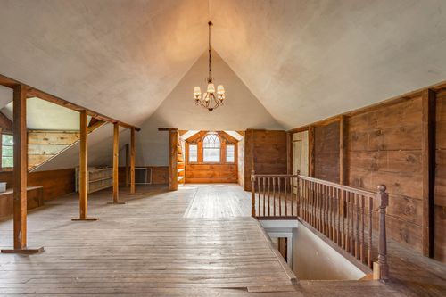 Open attic loft with vaulted plaster ceiling, wood paneling, and a stair railing