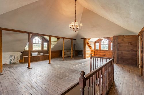 Rustic attic loft with arched windows, wood paneling, and a hanging chandelier