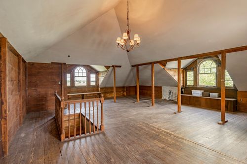 Spacious attic loft with exposed wood beams, arched windows, and a chandelier