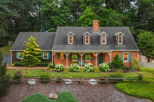 Aerial view of a brick cape cod home with dormer windows and lush landscaping