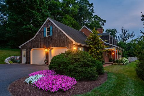 Backyard pool lit at dusk with a stone patio, string lights, and Adirondack chairs