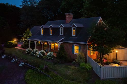 Aerial twilight view of a brick cape cod home with dormers and garden beds