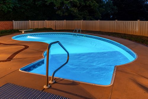 Nighttime view of an illuminated pool with handrail steps and a tan patio