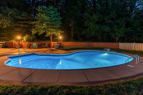 Nighttime pool view with string lights, a brick wall, and lounge chairs on the patio